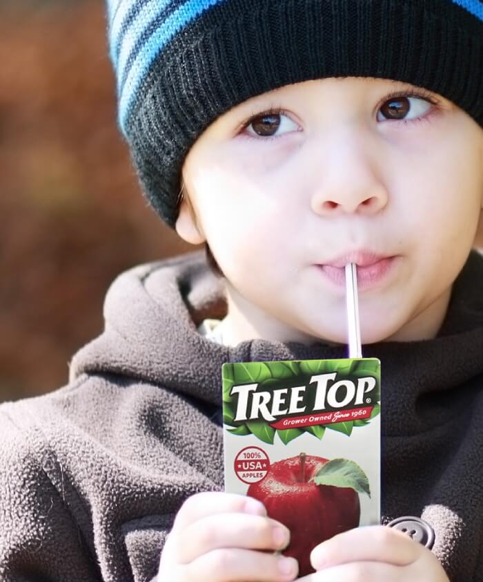 Young boy enjoying box of Treetop apple juice.