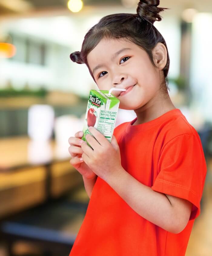 Girl drinking from Treetop juice box.